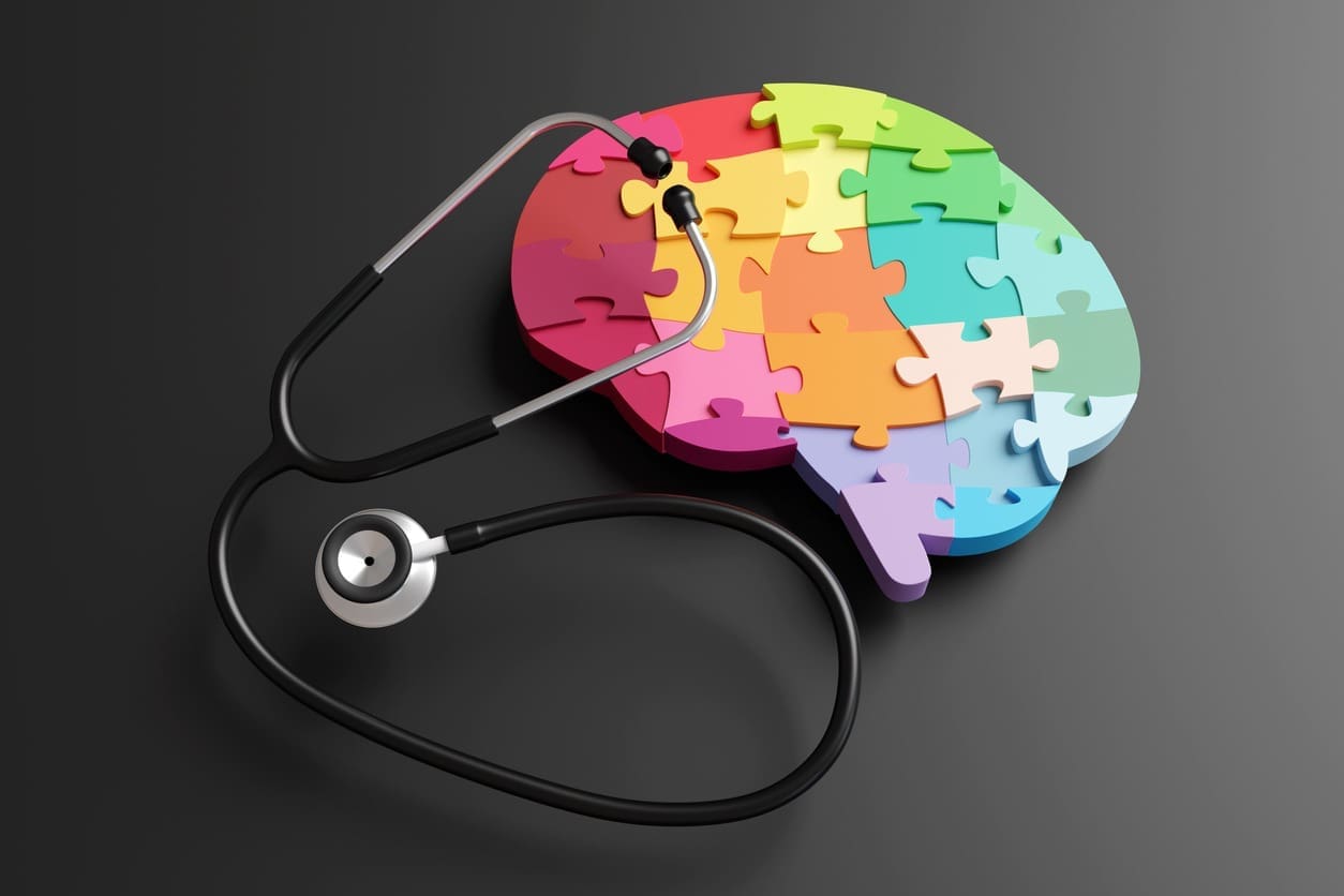 A stethoscope rests on a colorful brain-shaped puzzle, symbolizing the connection between mental health and medical care, on a dark background.
